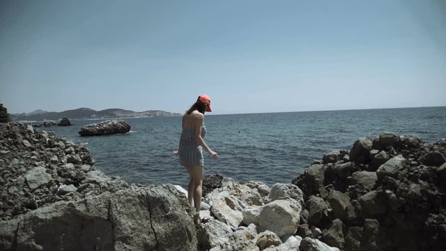 Girl stand on rough stones of sea shore and look at high rise building construction on other harbor side