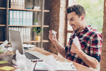 Side profile shot of frustrated young brunet entrepreneur,  yelling at his laptop in office and...