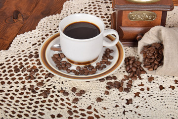 Grains of freshly ground coffee in a bag next to a cup of hot black coffee