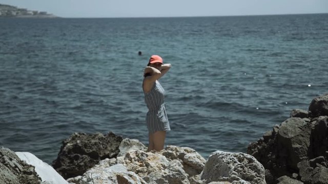 Girl stand on rough stones of sea shore and look at high rise building construction on other harbor side