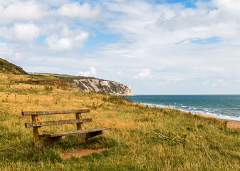 Old worn wooden bench looks out over the sea in Sandown Bay on the Isle of Wight with Culver cliff and Red Cliff in the background. The sky is cloudy, but it is still a romantic location.