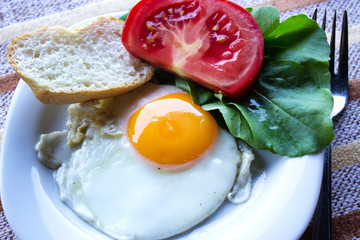 Fried egg on a plate with tomato and lettuce leaves. Selective focus. Horizontal.