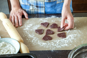 a woman in a home kitchen makes dough to bake cookies, cuts out chocolate dough cookies in the form of a heart