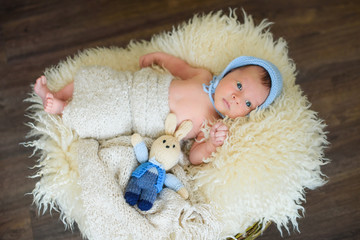 likable and pretty newborn baby boy with big blue eyes in a knitted hat on a wooden background at home