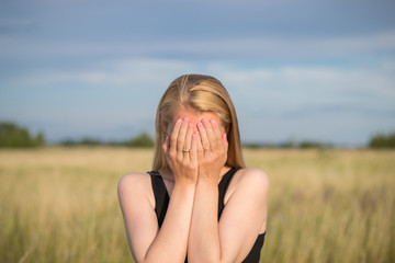blonde girl in depression covers her face with her hands on the outdoor