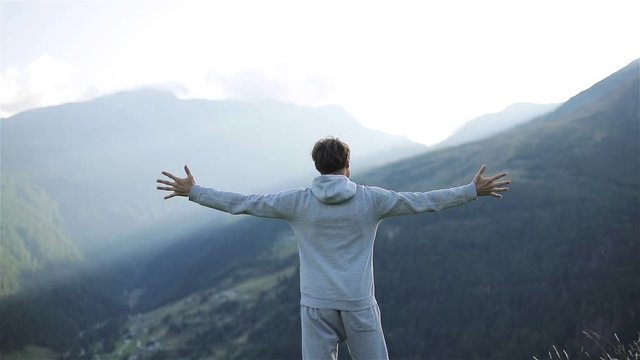 Man raises hands up standing back on mountain top morning sun shine slow motion. No face male silhouette figure in sportswear enjoying life above world. Achievement success motivation winner concept