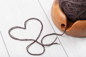 knitting with a wool yarn ball in a wooden bowl on a white oak desk floor, heart shape from the...