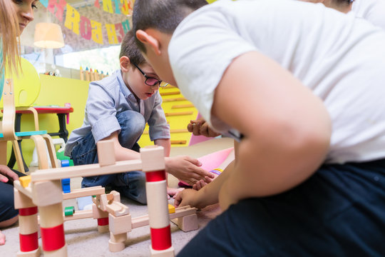 Cute boy wearing eyeglasses while building with attention and patience a wooden structure during an educational group activity at the kindergarten