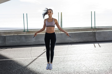 Young fit woman skipping with a jump rope in the city, full length 