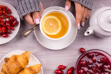 Woman's hand holding cup of tea with lemon on a cold autumn or winter day