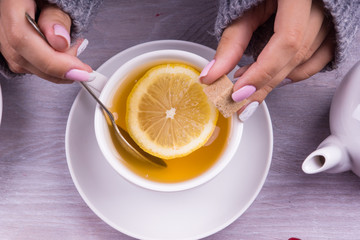 Woman's hand holding cup of tea with lemon on a cold autumn or winter day