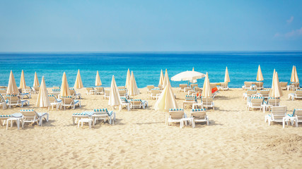 Resort beach with white sand. Tropical summer vacation. Sun beds and umbrellas on beach against blue sea and sky