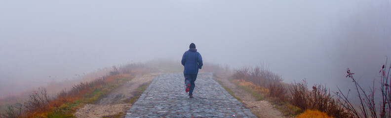 Man running on cobblestone on foggy dark day