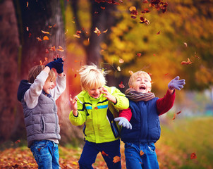 happy friends, schoolchildren having fun in autumn park among fallen leaves