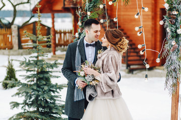 Groom tenderly embracing her beautiful bride. Winter wedding ceremony in rustic style outdoors....