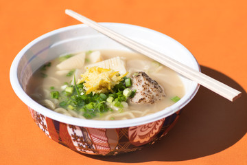 Japanese taste ramen soup with noodles,green onion,meat, served in bowl and wooden sticks on the table with orange tablecloth.