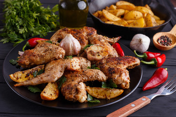 Grilled chicken wings on black plate decorated with garlic, lemon slices and chili peppers. Cooking concept, meat dishes, homemade food