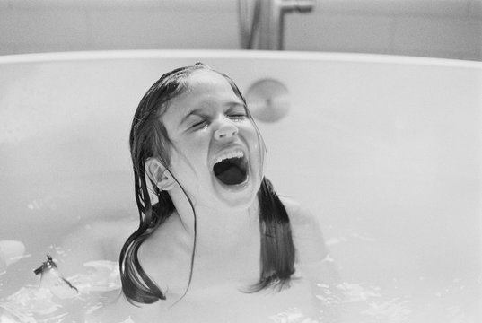 Cute young girl screaming of joy in a bath tub
