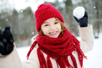 Adorable little girl having fun in beautiful winter park. Cute child playing in a snow. © MNStudio