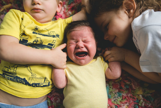 Unhappy baby surrounded by siblings