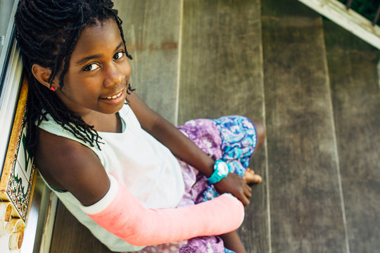 African-American girl with pink cast sitting on steps
