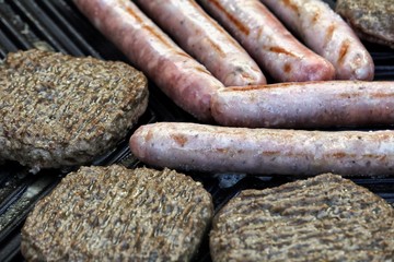 Close up of sausages and burgers sizzling on a barbecue griddle plate