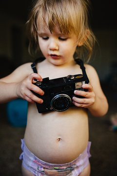 Toddler girl playing with an old camera.
