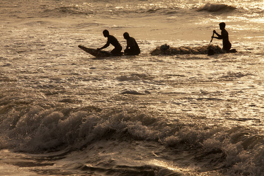 Silhouette of fishermen struggling with small boat to come near sea shore