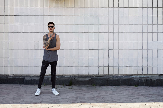 Young man with tattoos in sunglasses against of white ceramic wall