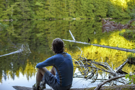 A man sits on a log next to Cedar Lake in Bellingham, Washington