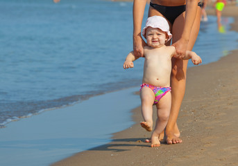 Naklejka premium Mom teaches her daughter to walk to the beach.