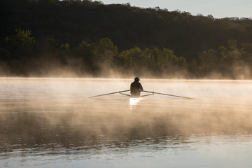 Silhouetted Man Sculling at Sunrise on Water with Fog © Isabelle
