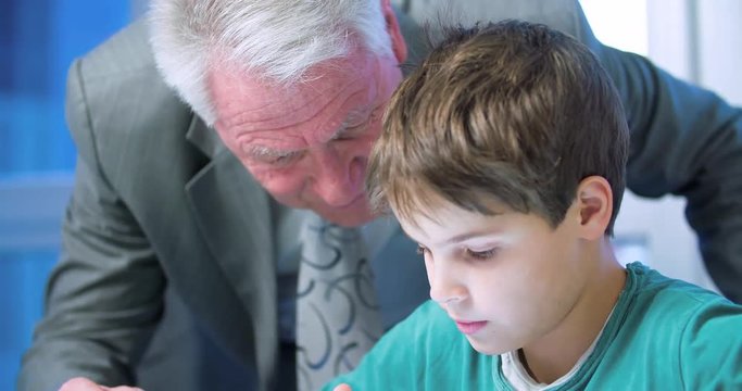 Grandfather and grandson child use a tablet 4k video. Old man and boy kid touch mobile PC screen. Family, technology and education