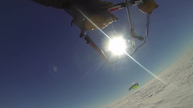 A shot from a gopro attached to a parasailer. The person is parasailing on snow under a sunny day.