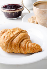 Traditional breakfast with fresh croissants and coffee on white wooden background.