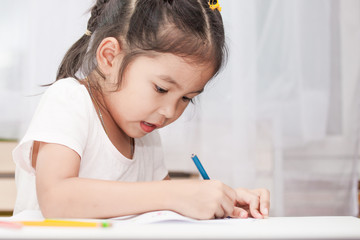 Cute asian child girl having fun to draw and paint with crayon in the room