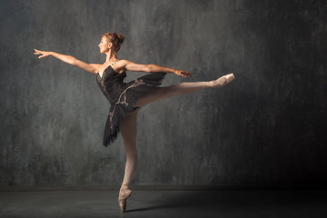 Fototapeta na wymiar A young beautiful ballerina in a scenic tutu, white pantyhose and pointe shoes beautifully poses and dances the ballet in the form of a dark swan in a dark dance stage