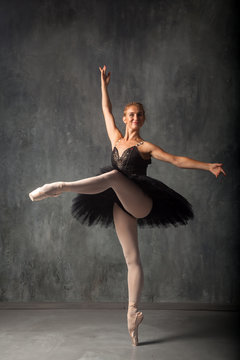 A young beautiful ballerina in a scenic tutu, white pantyhose and pointe shoes beautifully poses and dances the ballet in the form of a dark swan in a dark dance stage