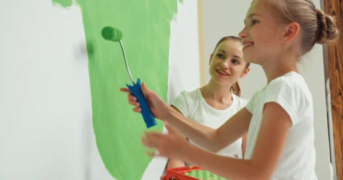 Mather and daughter together painting wall in color green and smiling at camera