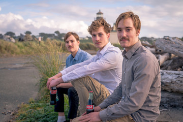 Portrait of three friends sitting on a log outdoors by a lighthouse

