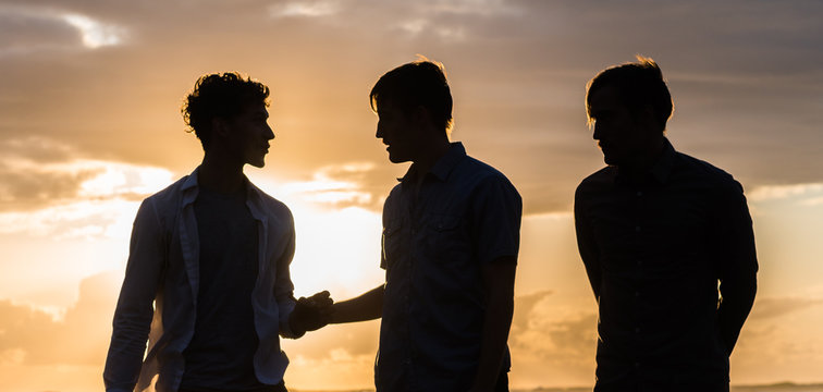 Silhouette Of Three Young Men At The Beach At Sunset