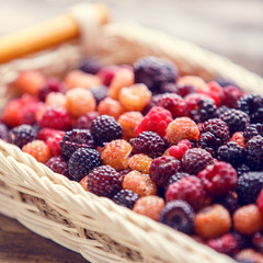 Close up image of wild berries in wicker basket on wooden table. Warm color toned image