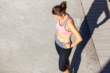 Young slim girl resting after run training in the park. Smiling runner woman standing outdoors