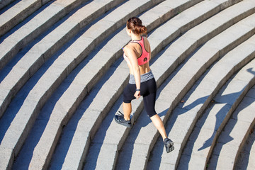 Young slim woman in pink top running on stairs in the morning city. Healthy lifestyle background with copyspace