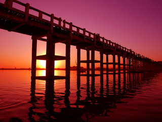 Fototapeta na wymiar Beautiful sunset behind a long wooden bridge in Mandalay, Myanmar in red tone