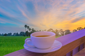Abstract soft focus a cup of cappuccino, hot coffee with soft blurred  silhouette the sunset ,green paddy rice field , beautiful sky and cloud in Thailand. By the beam,light and lens flare effect tone