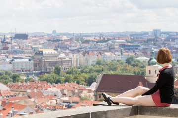 Fototapeta na wymiar Prague, Czech Republic - August 19, 2017: Asian girl are sitting on a wall of a balcony with panoramic city views