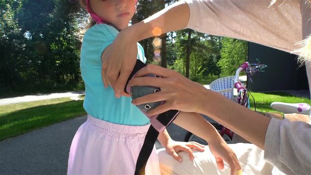 Careful mother helps her little daughter to wear protective elbow pads and gloves. Slow motion