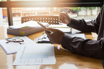 Business and finance concept of office working, Businessman using smartphone to calculate and discussing analysis chart