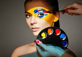 Makeup artist applies colorful makeup. Fashion model woman with colored face painted. Beauty art...
